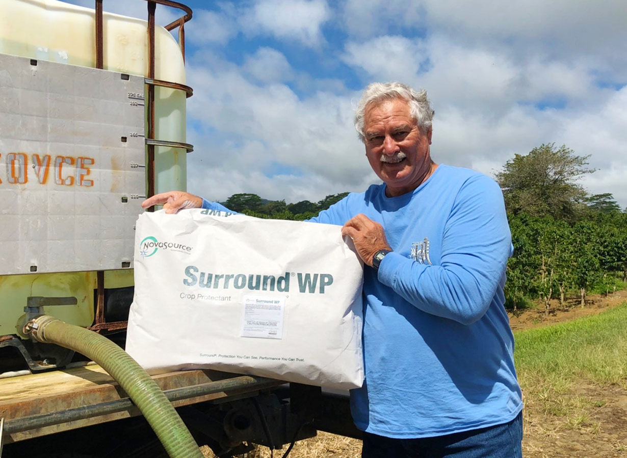 Farm owner John holding a bag of the white clay sprayed on the leaves, in front of the farm's tank truck