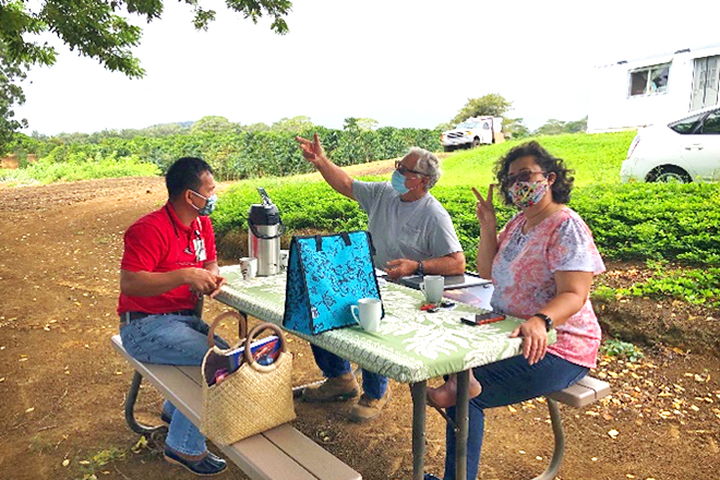 Farm owner John sitting across from the Hawaii Department of Agriculture inspector at an outdoor table on the farm