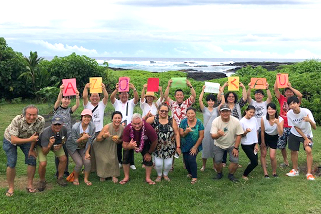 海岸沿いの草地で「Aloha from Ka'u」の文字を掲げて並ぶ参加者たち
