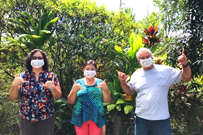 「ALOHA」「FROM」「KAU」と書いたマスクを着けて並ぶ3人と、背後に茂るハワイの植物